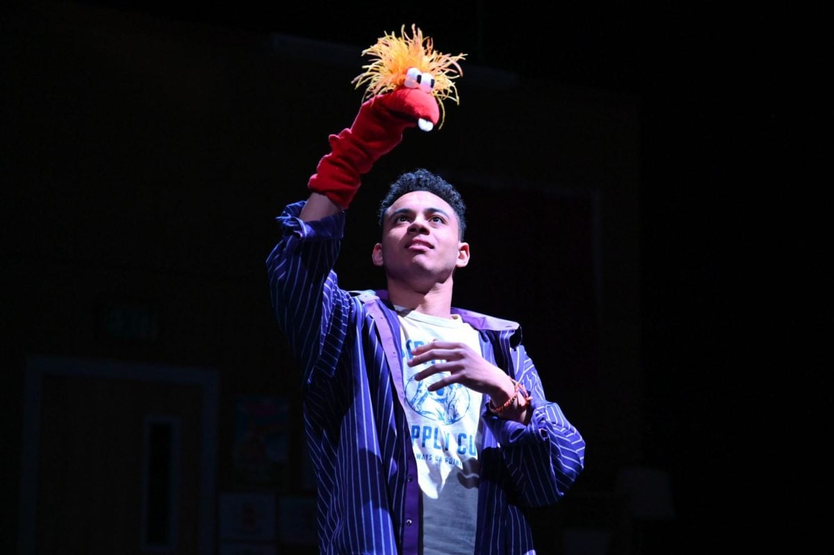 A young man with a sock puppet on his hand, reaching up